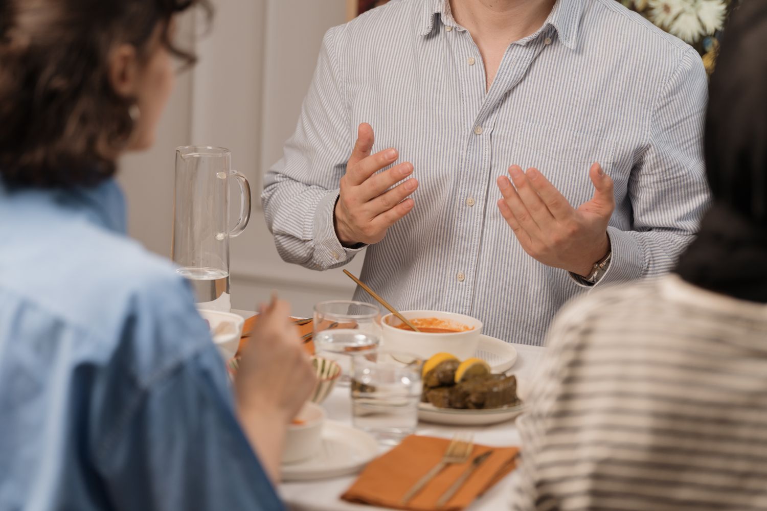 A family talks across a kitchen table over a meal while one man explains something with both hands.